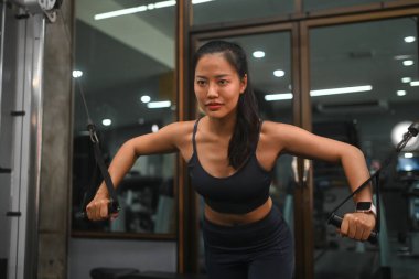 Fitness salonunda kablo sineği egzersizi yapan zinde genç bir kadın. Sağlıklı ve aktif yaşam tarzı kavramı.