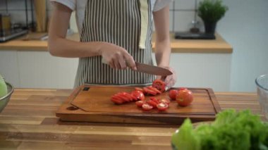 Genç bir kadın domatesleri tahta kesme tahtasıyla doğruyor mutfakta sağlıklı bir yemek hazırlıyor..