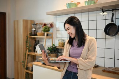 Mutfakta dizüstü bilgisayar kullanan genç ve güzel bir kadın..