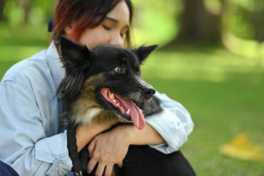 Gülümseyen genç kadın çimenlerde dinleniyor ve köpeğini sevgiyle kucaklıyor..