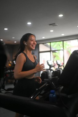 Müzik dinleyen ve spor salonunda koşu bandında koşan mutlu bir atletik kadın..