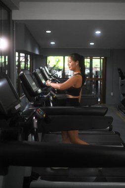 Genç atletik kadın spor salonunda koşu bandında yürürken nabzını kontrol ediyor..