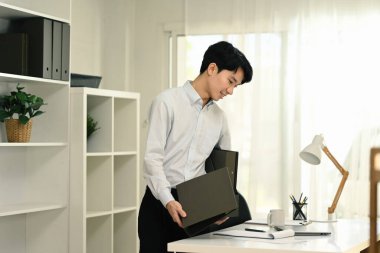 Gülümseyen genç işadamı taşınma gününde yeni ofiste kutuları açıyor..