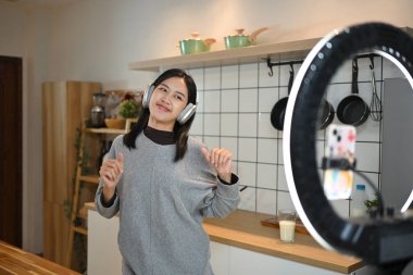 Neşeli genç bir kadın mutfakta dans ederken kendini akıllı telefonuyla kaydediyor..