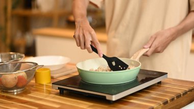 Bir adamın karıştırmak ve pişirmek için bir spatula kullanarak yakın çekim Bir indüksiyon soba içinde kızartma tavasında malzemeler.