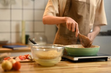 Bir adamın karıştırmak ve pişirmek için bir spatula kullanarak yakın çekim Bir indüksiyon soba içinde kızartma tavasında malzemeler.