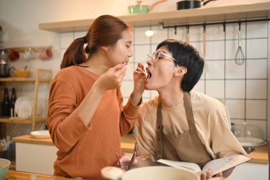 Genç bir çift, sıcak bir mutfakta aynı spagettiyi yerken neşeli bir yemek pişirme anı yaşıyor..