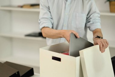Genç erkek ofis çalışanı kovulduktan sonra eşyalarını kutuya koyuyor..