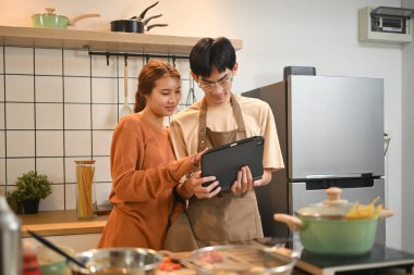 Genç Asyalı aşçı çift mutfakta yemek pişiriyor ve dijital tabletten yemek tariflerine bakıyor..