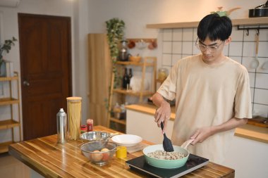 Genç adam spatulayla yeşil bir tavada malzemeleri karıştırıyor. İnsanlar, yemek ve yaşam tarzı konsepti.