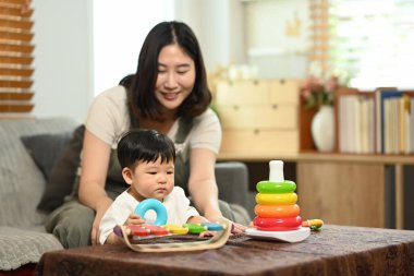 Sevimli küçük bir çocuk ve anne sıcak bir oturma odasında renkli oyuncaklarla oynuyorlar..