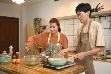 Sıcak bir mutfakta yemek pişiren önlük giyen genç bir çift. İlişkiler, yemek pişirme ve mutlu bir ev hayatı..