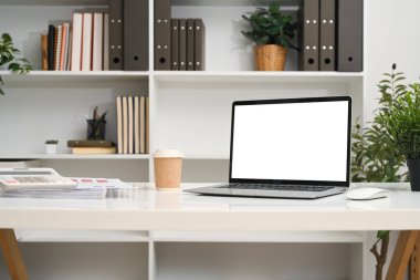 Boş ekran ve ofis malzemeleriyle dolu bir dizüstü bilgisayar bir kitaplığın önündeki masada..