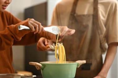 Sıcak bir mutfakta yemek pişiren önlük giyen genç bir çift. İlişkiler, yemek pişirme ve mutlu bir ev hayatı..