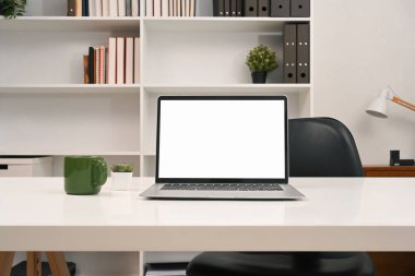 Boş ekran ve ofis malzemeleriyle dolu bir dizüstü bilgisayar bir kitaplığın önündeki masada..