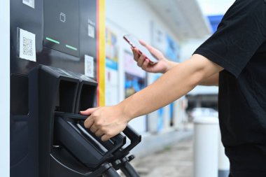 Akıllı telefonlu QR kodunu tarayan adam şarj istasyonunda şarj edilen elektrikli araba aküsüne ödeme yapıyor..