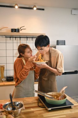 Önlük takan, birlikte yemek pişirmekten ve sıcak bir mutfakta yemek yemekten hoşlanan mutlu genç bir çift..