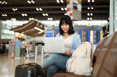 Havaalanı terminalinde dizüstü bilgisayar kullanan güzel bir kadın uçağını bekliyor..