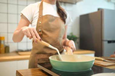 Genç bir kadının yemek pişirme sahnesi, kızartma tavasında spatulayla karıştırma malzemeleri..