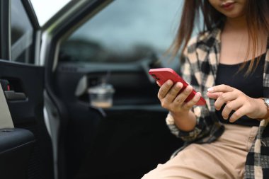 Kapısı açık arabada oturan turist kadının cep telefonu kullanırken görüntüsü..