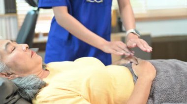 Huzurlu, gözleri kapalı yaşlı bir kadın terapistle Reiki 'nin tedavisini görüyor. Alternatif tıp konsepti.