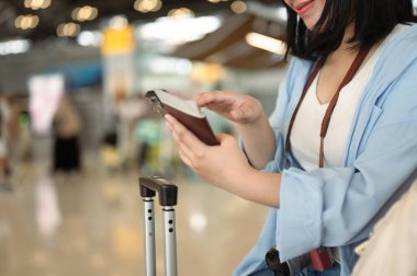 Pasaportu olan ve havaalanında uçuş bilgilerini kontrol etmek için cep telefonu kullanan genç bir kadın..