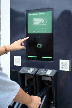 Şarj istasyonunun dokunmatik ekran arayüzü ile etkileşime giren genç kadın.