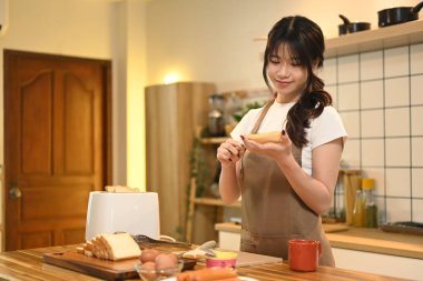 Genç bir kadın öğle yemeği için sandviç yapıyor ve ekmeğe bıçakla tereyağı sürüyor..