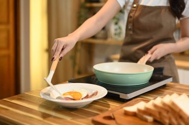 Genç bir kadın mutfakta duruyor ve bir tabakta kızarmış yumurta ve pastırma servis ediyor..