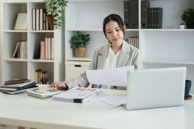 Çekici kadın muhasebeci belgeleri inceliyor ve masada hesap makinesi kullanıyor..
