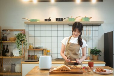 Gülümseyen Asyalı kadın, sıcak bir mutfakta kahvaltı hazırlıyor..