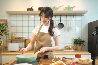 Güzel genç bir kadın, mutfakta kahvaltı hazırlarken tavaya yumurta kırıyor..