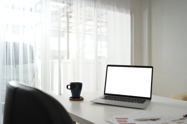 Boş ekranlı dizüstü bilgisayar, finansal belgeler ve beyaz masada bir fincan kahve..