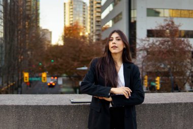 Sonbahar yeşillikleriyle modern bir binanın önünde duran kendine güvenen İspanyol iş kadını..