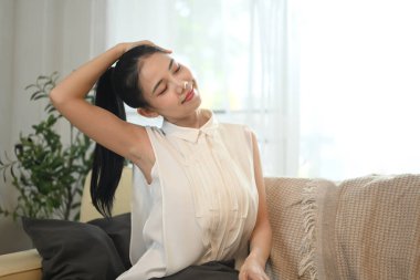 Gülümseyen genç bir kadın evdeki kanepede oturuyor ve boynu kapalı bir şekilde uzanıyor..