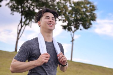 Gülümseyen Asyalı genç adam bulutlu bir günde parkta koşuyor. Fitness ve aktif yaşam tarzı.