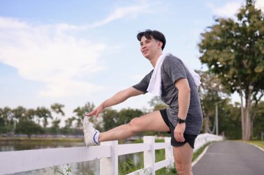 Beyaz bir çitin üzerinde bacağını esneten yakışıklı sporcu egzersize hazırlanıyor. Fitness ve sağlıklı yaşam konsepti.