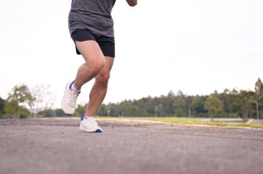 Erkek koşucu bacakları dışarıda asfalt bir yol boyunca hareket ediyor. Fitness ve aktif yaşam tarzı.