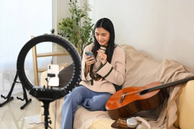 Kadın içerik oluşturucu telefonu kontrol ediyor ve evde bir müzik videosu kaydetmek için kurulum yapıyor.