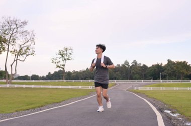 Gülümseyen genç sporcu doğayla çevrili bir yolda koşuyor..