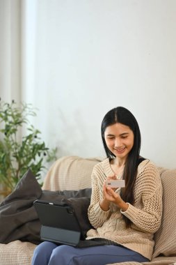 Evden alışveriş yapmak için kredi kartı kullanan mutlu bir kadın..