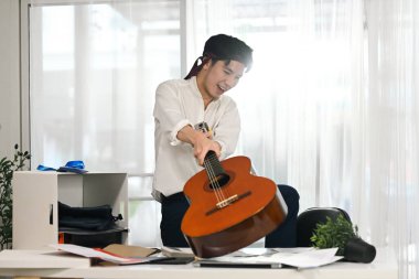 Öfkeli erkek çalışanın ofis masasında gitar kırması..