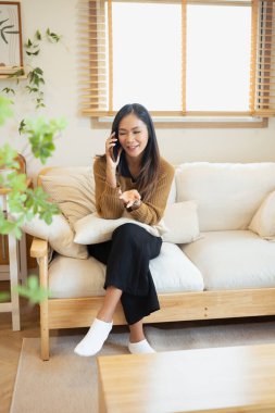 Güzel bir Asyalı kadın oturma odasında cep telefonuyla konuşuyor..
