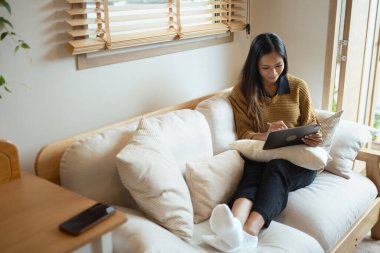 Oturma odasında dijital tablet kullanan gülümseyen genç kadın..