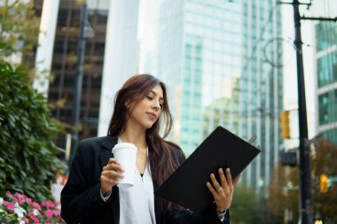 İş kadını modern şehir manzarasında kahve molası sırasında iş belgelerini inceliyor.
