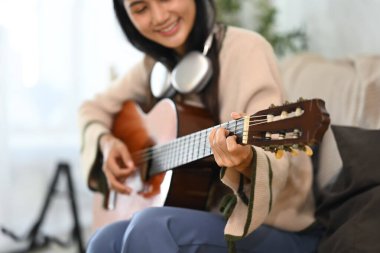 Genç ve güzel bir kadın oturma odasında akustik gitar çalıyor..