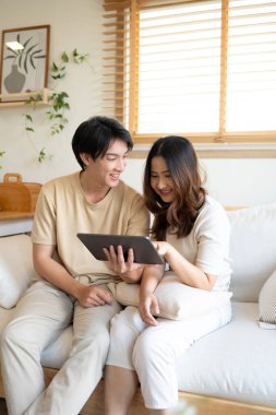 Gülümseyen genç çift evdeki kanepede dijital tabletle rahatlıyor..