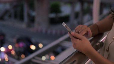 Akşamları şehir manzarası bulanık bir şekilde akıllı telefondan yazı yazan kadına yaklaş..