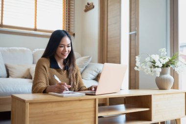 Bilgisayarla uzaktan çalışan ve notlar yazan alımlı genç bir kadın..