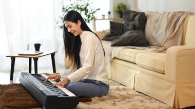 Gülümseyen genç kadın oturma odasında elektrikli piyano çalışıyor..